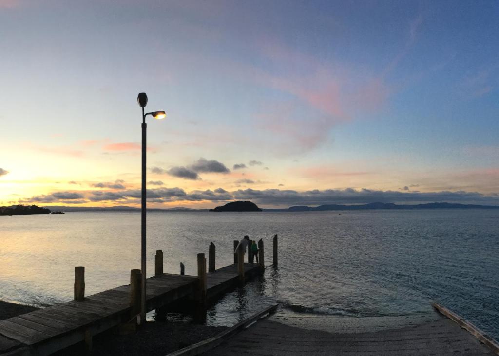 two people standing on a dock in the water at sunset at Motutere Bay TOP 10 Holiday Park in Turangi