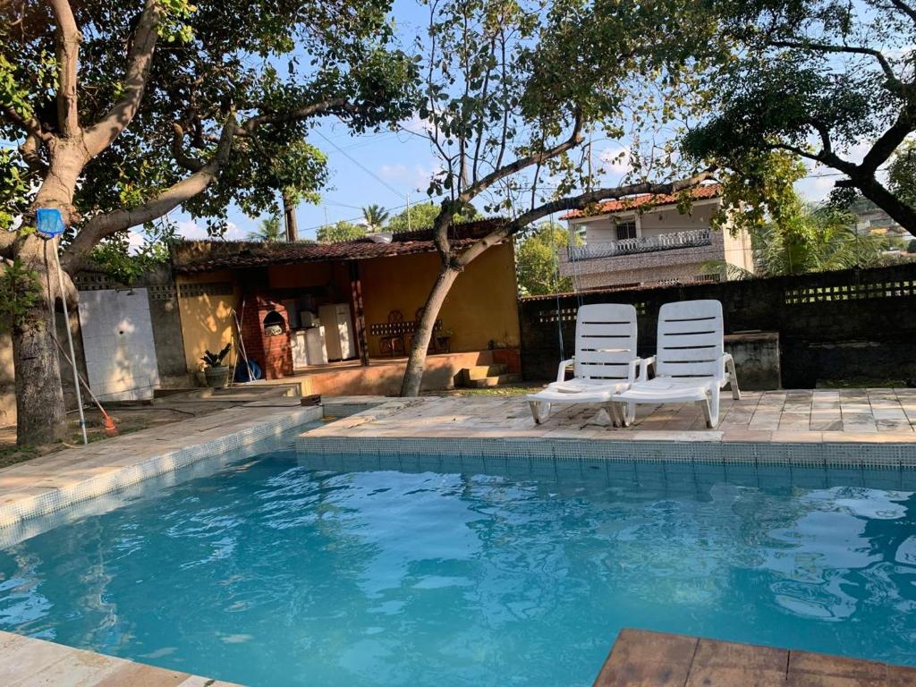 two white chairs sitting next to a swimming pool at Casa de praia Itamaracá in Itamaracá