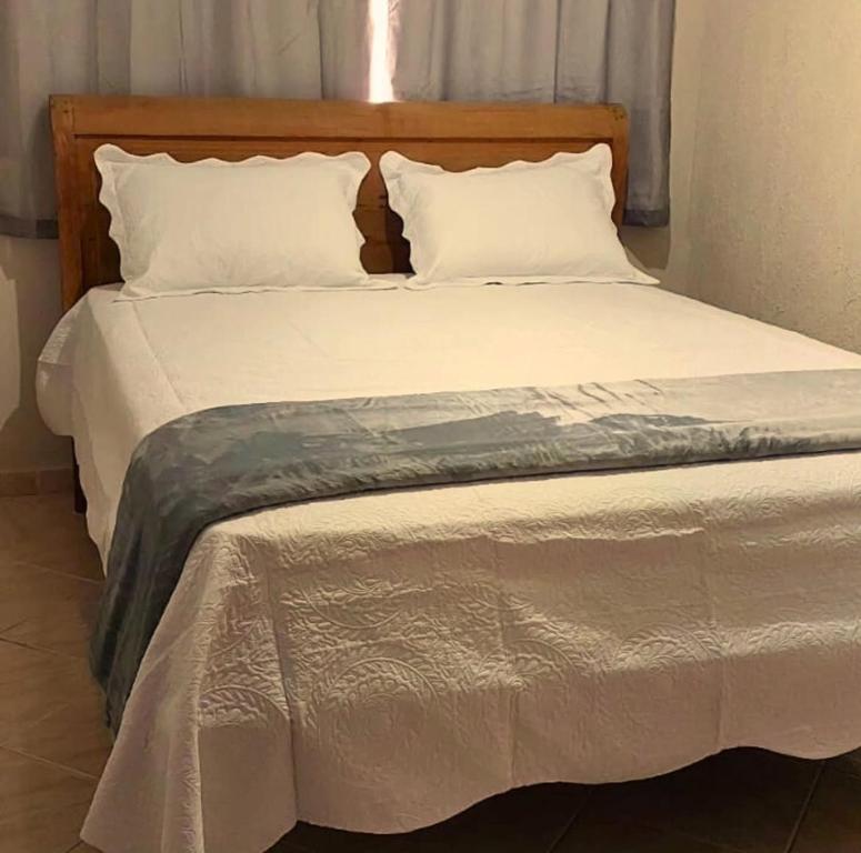 Elle comprend un grand lit avec des draps et des oreillers blancs. dans l'établissement Hospedagem cama e café, à Domingos Martins