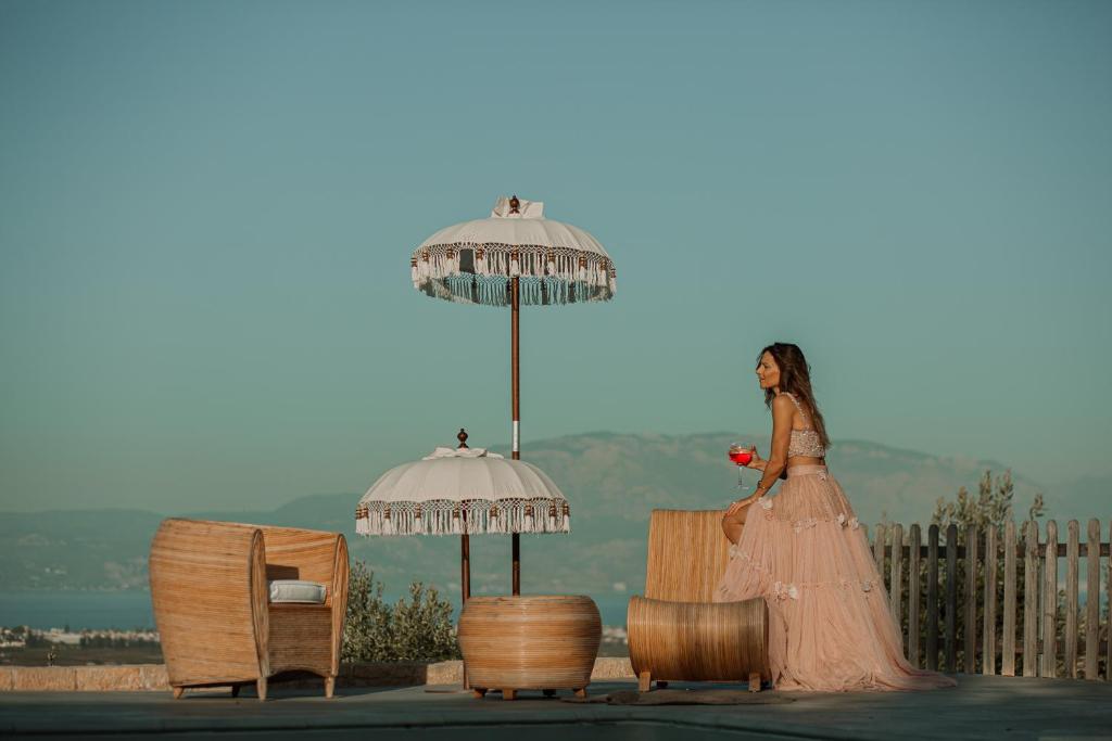 a woman in a dress standing next to chairs and umbrellas at Arion Hotel in Kórinthos