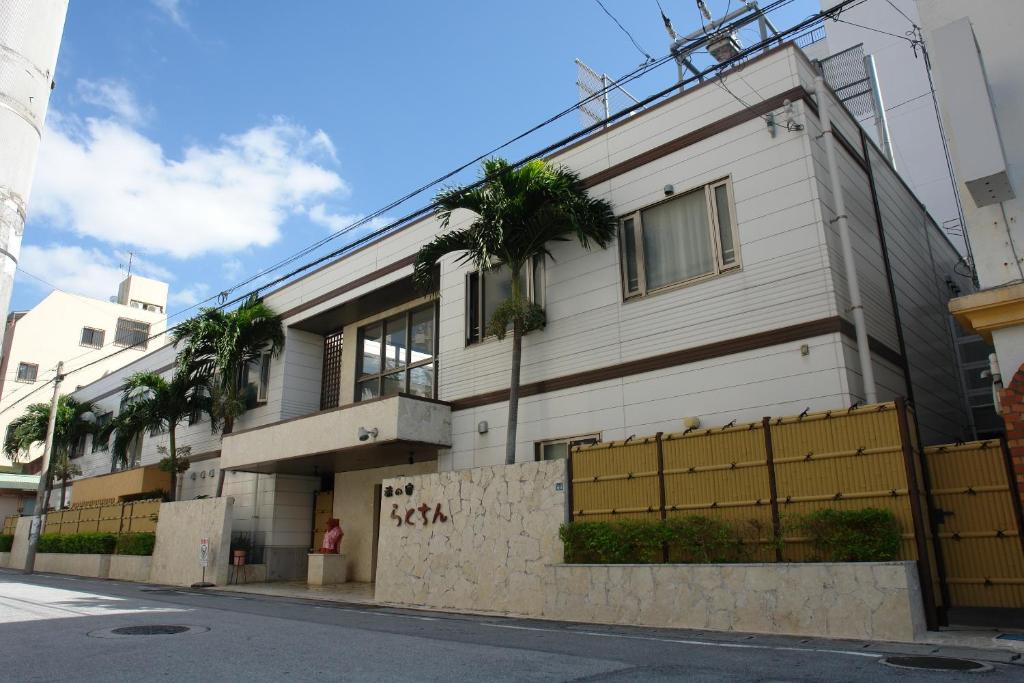 a white building with palm trees on a street at Rakuchin in Naha
