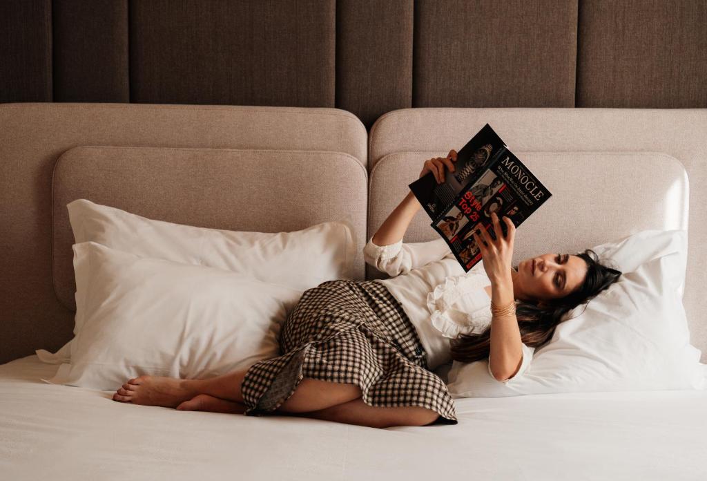 een vrouw die op een bed ligt en een boek leest bij The Log Porto Hotel by Piamonte Hotels in Porto