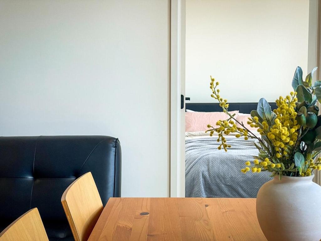 a room with a table with a vase with yellow flowers at Mcity Morden 2BR with Free Parking in Clayton North