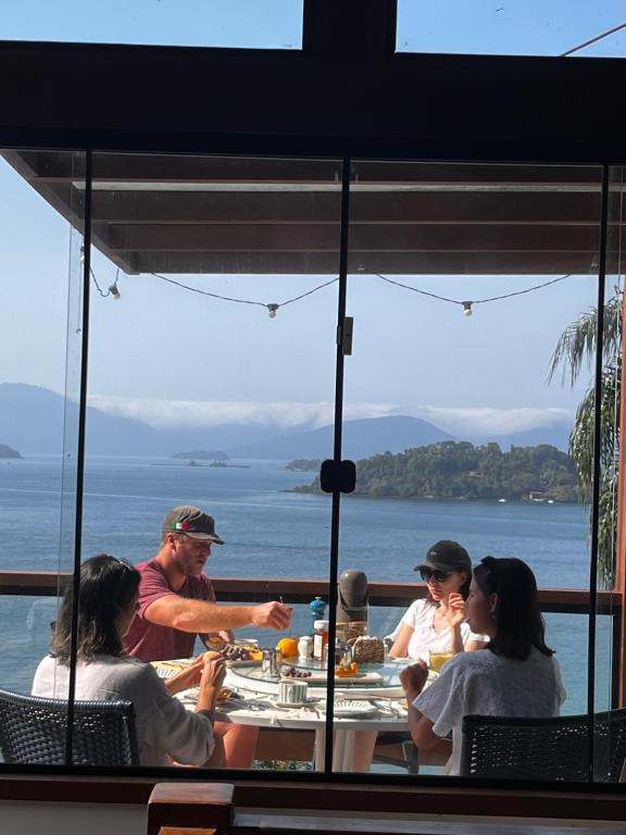 een groep mensen die aan een tafel zitten met uitzicht op de oceaan bij Casa Botanique in Angra dos Reis