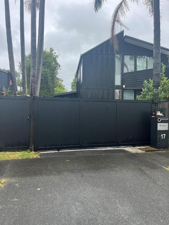 a black fence in front of a house with palm trees at Myrtle St Guesthouse in Auckland
