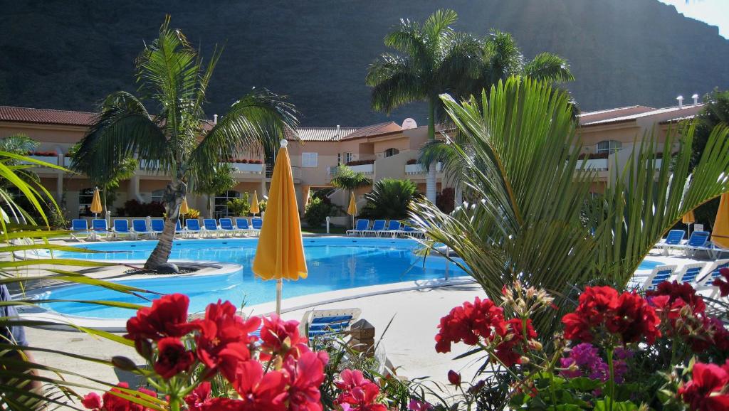 een zwembad van het hotel met een gele parasol en palmbomen bij Apartamentos Jardín del Conde in Valle Gran Rey