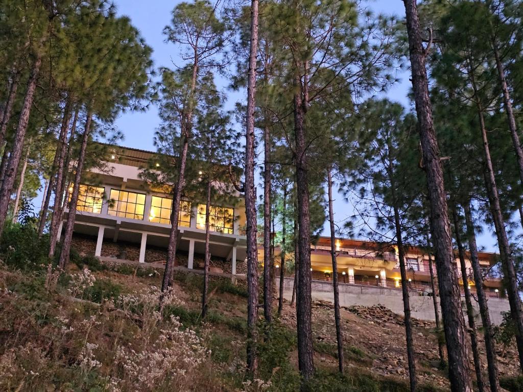 un bâtiment dans les bois avec des arbres au premier plan dans l'établissement ilika Resort, Pauri, à Pauri