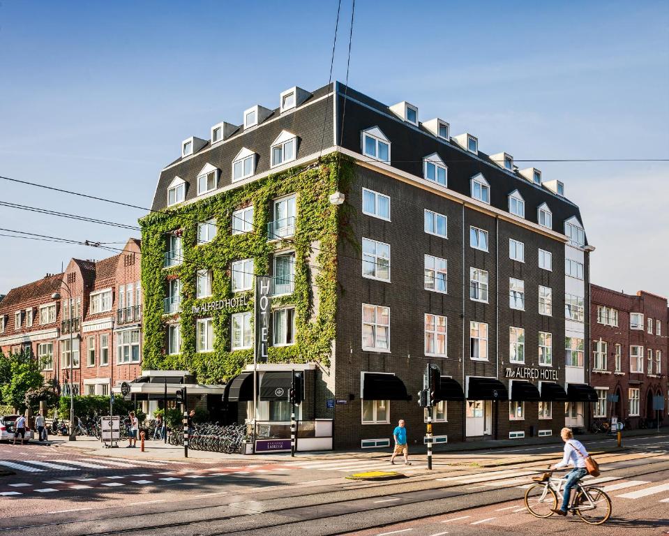 een persoon die fietst voor een gebouw bij The Alfred Hotel in Amsterdam