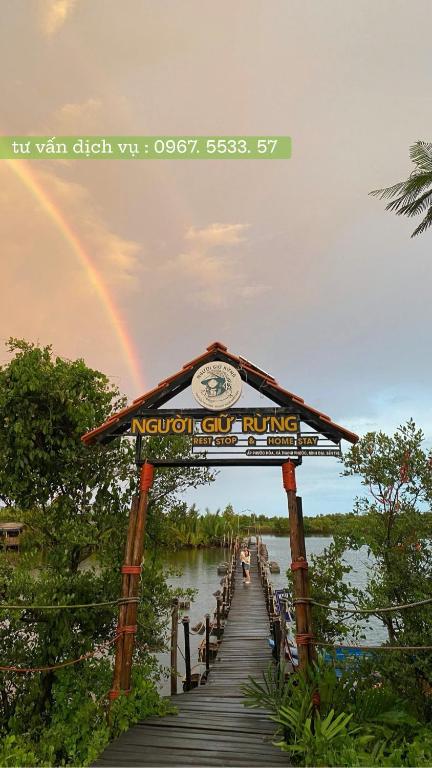 a boardwalk with a clock and a rainbow in the background at Người Giữ Rừng- Nhà hàng và Du Lịch Sinh Thái in Bình Ðại