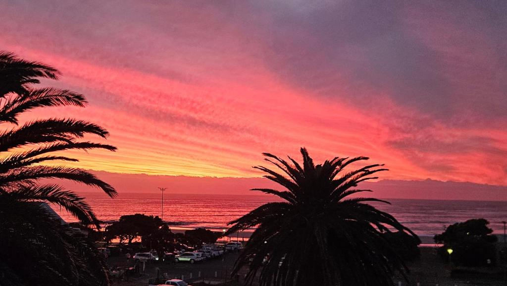 a sunset over a beach with palm trees and the ocean at Modern Sea and Mountain View Apartment - Gordon's Bay in Gordonʼs Bay