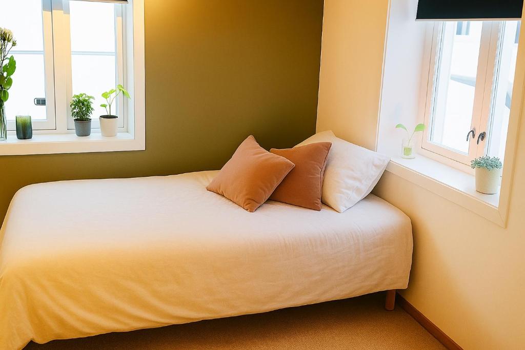 een bed met 2 kussens in een kamer met 2 ramen bij Cottage studio in city centre in Tromsø