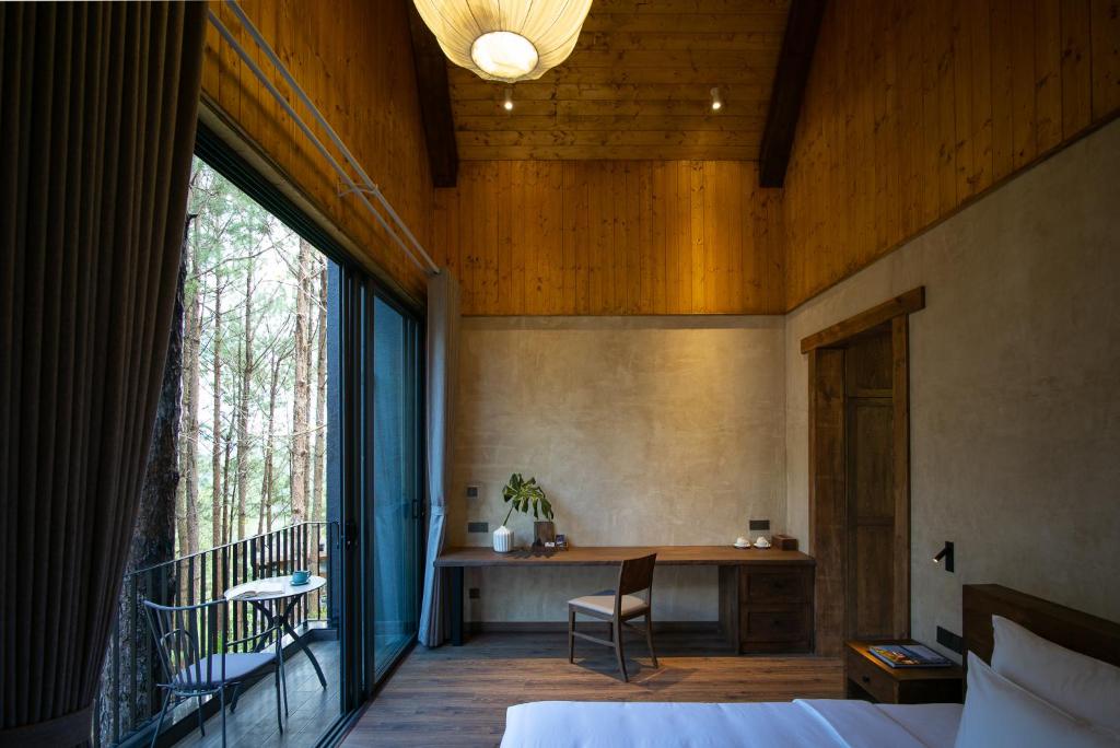 a bedroom with a bed and a desk and a window at Mơ Stay - Forest Resort in Da Lat