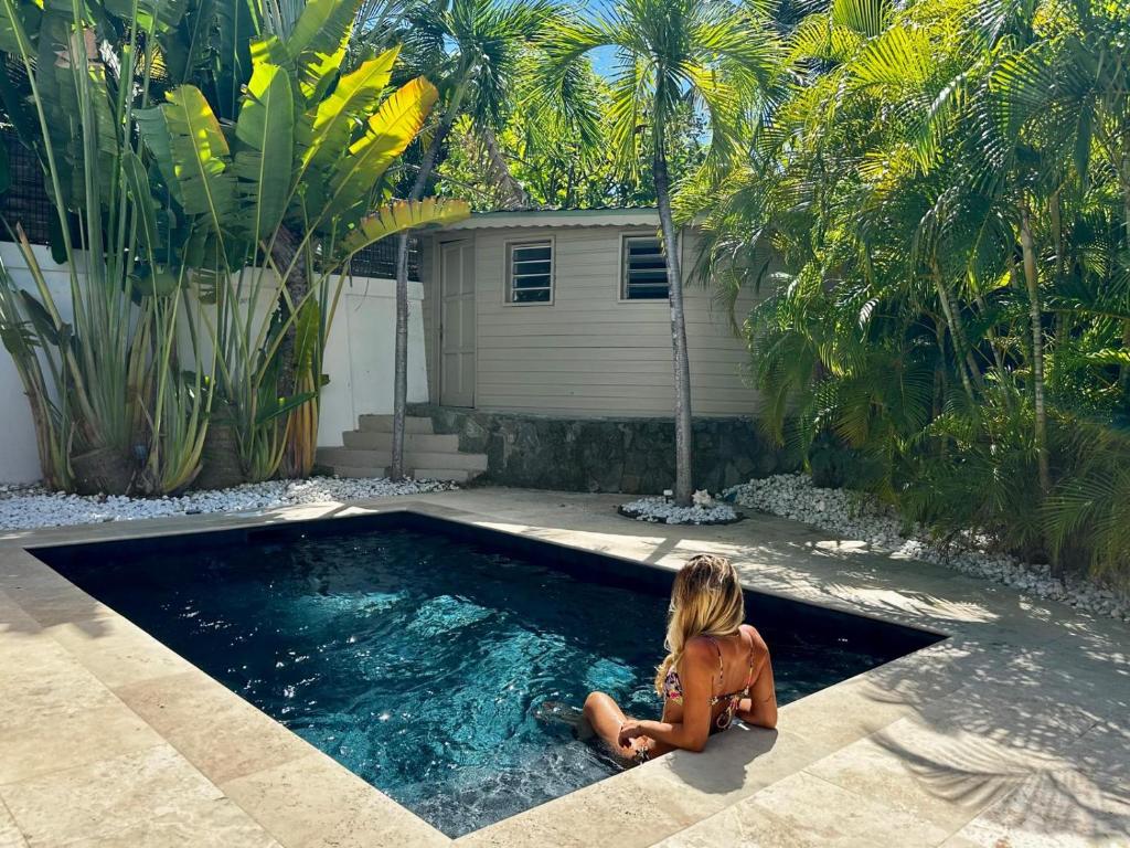 une femme assise dans une piscine à côté d'une maison dans l'établissement Mahi-Mahi Lodge, piscine privee, orient bay, à La Baie-Orientale