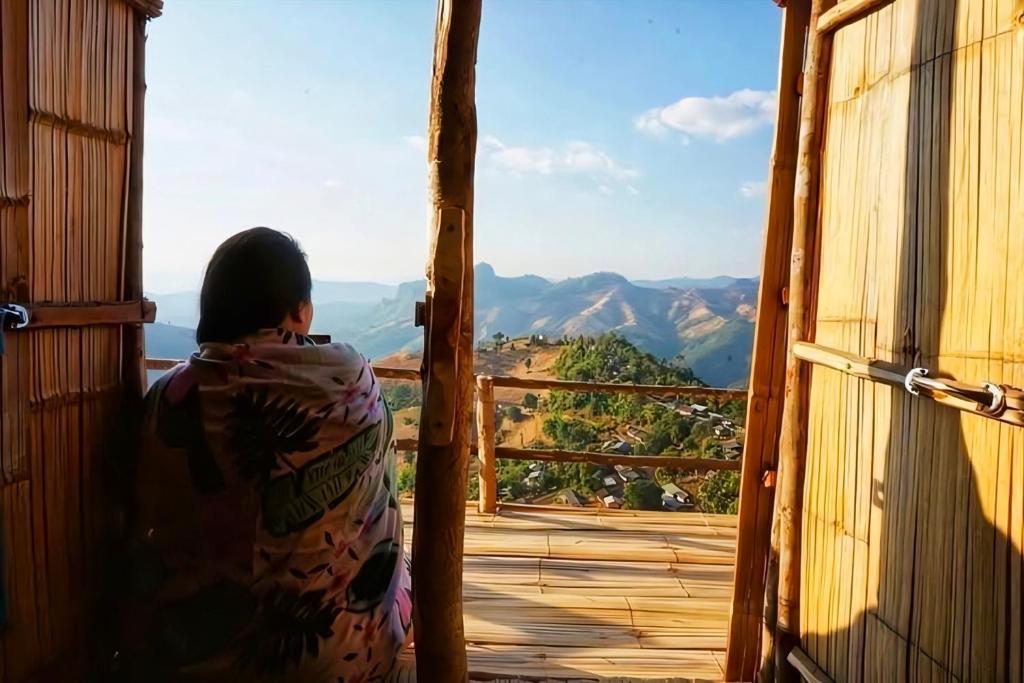une femme assise sur une terrasse couverte donnant sur les montagnes dans l'établissement Homestay Nunga หนูหง่าโฮมสเตย์, à Mae Hong Son
