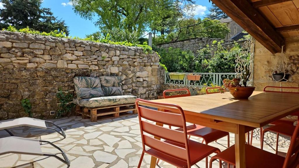 eine Terrasse mit einem Holztisch und Stühlen und einer Steinmauer in der Unterkunft Collias Bord du Gardon, near Uzès and Pont du Gard in Collias