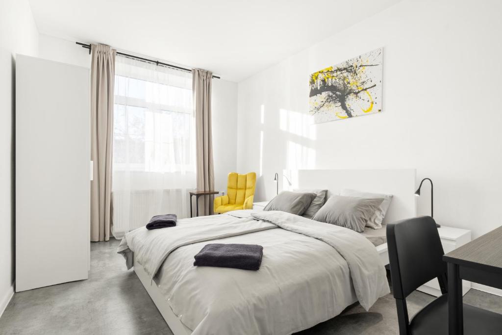 a white bedroom with a bed and a table and yellow chairs at SPECTRA Rooms in Velké Meziříčí