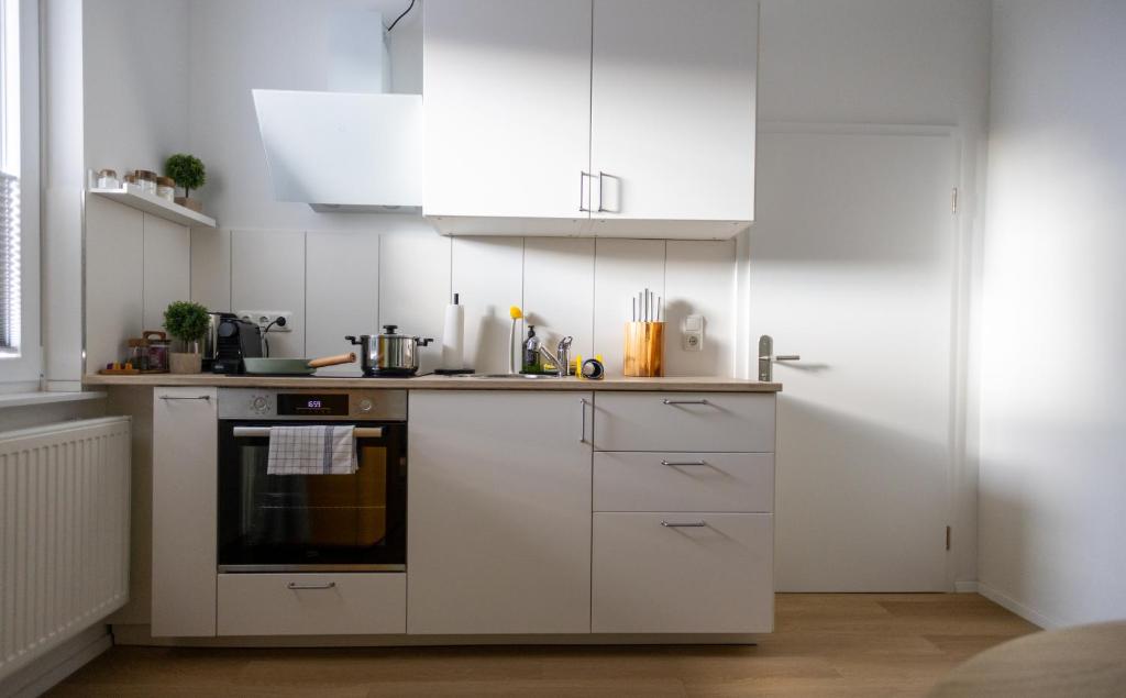 une cuisine avec des armoires blanches et un four à plaques de cuisson dans l'établissement Wohlfühl-Apartment Waldschimmer, Extra Komfort für Business & Urlaub, à Unterlüß