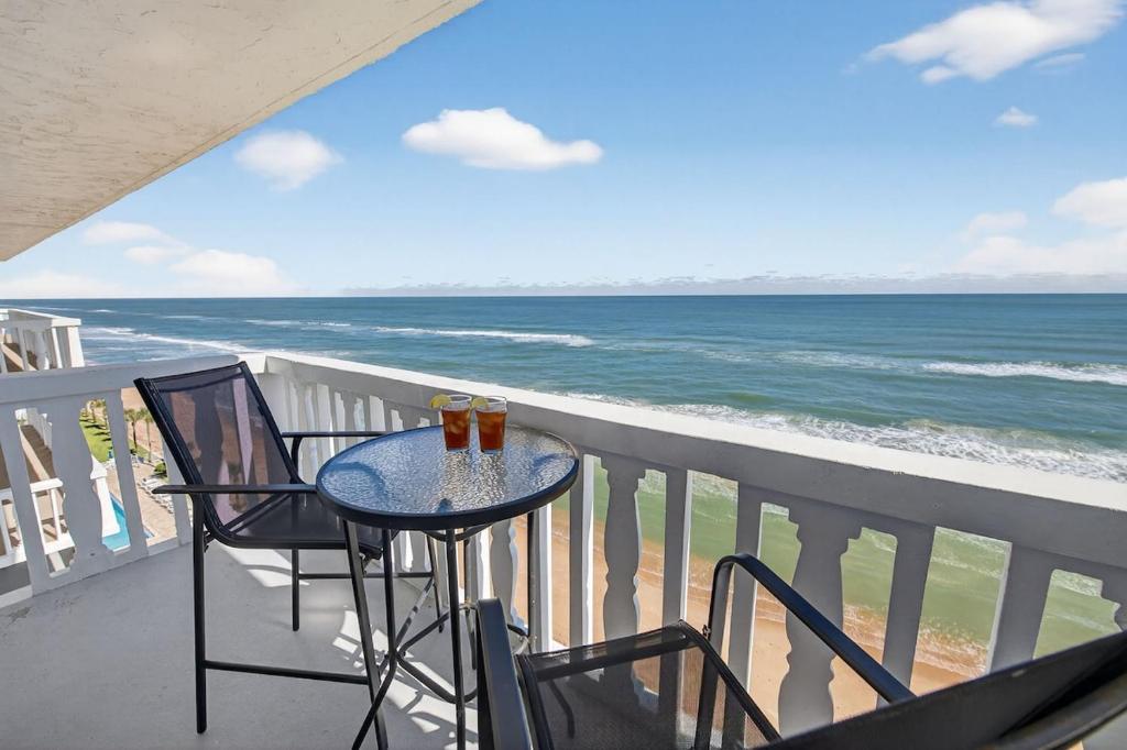 een balkon met een tafel en stoelen en de oceaan bij Ormond Beach Paradise - Steps from no-drive beach in Ormond Beach