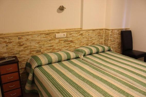 a bedroom with a bed with a green striped comforter at Hostal Valle del Iregua in Albelda de Iregua