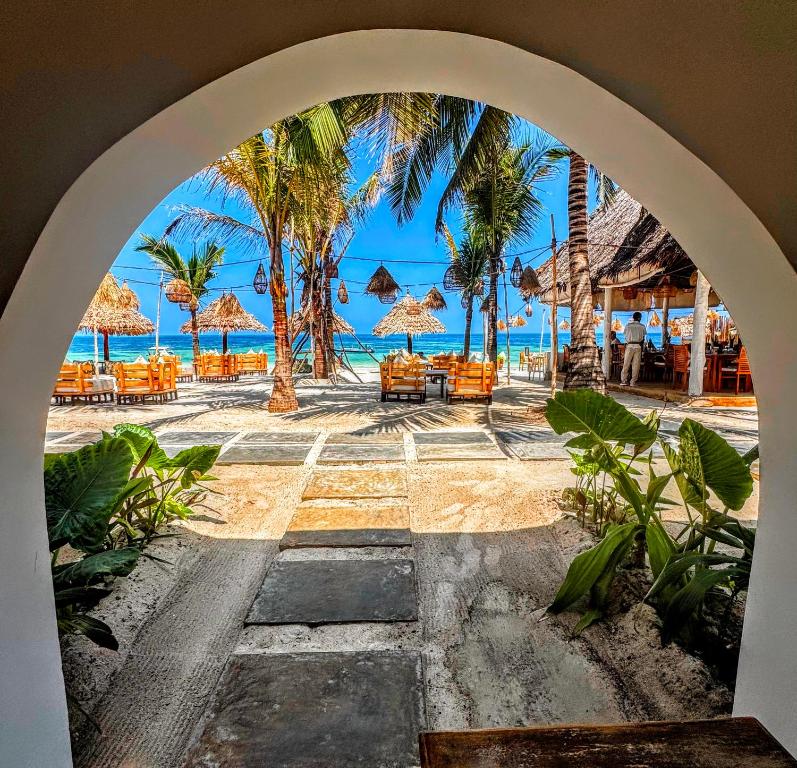 an archway leading to a beach with chairs and palm trees at Marea Boutique Hotel in Jambiani