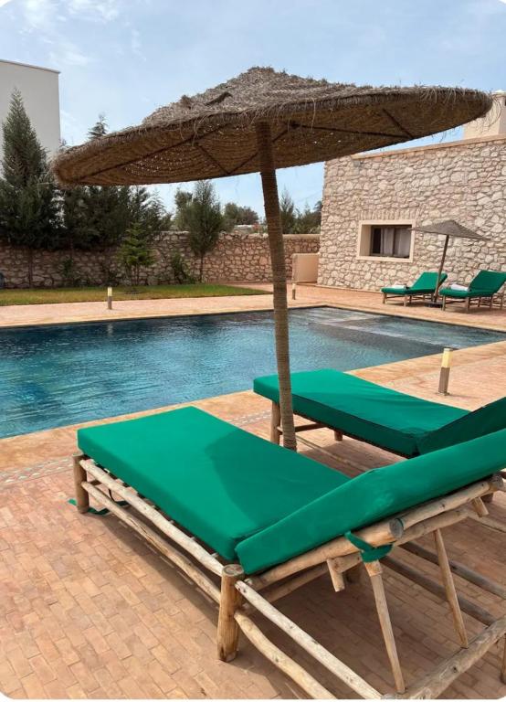 a pool with an umbrella and two lounge chairs at Igiwano guest house in Essaouira