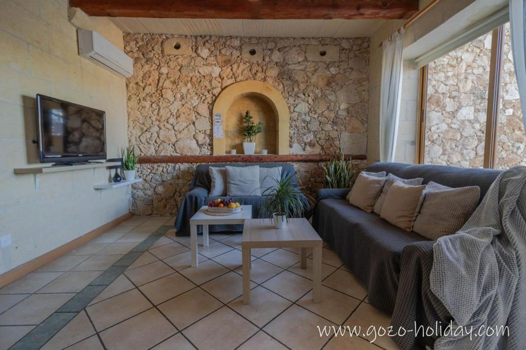 a living room with a blue couch and a stone wall at Hibiscus Xaghra in Xagħra