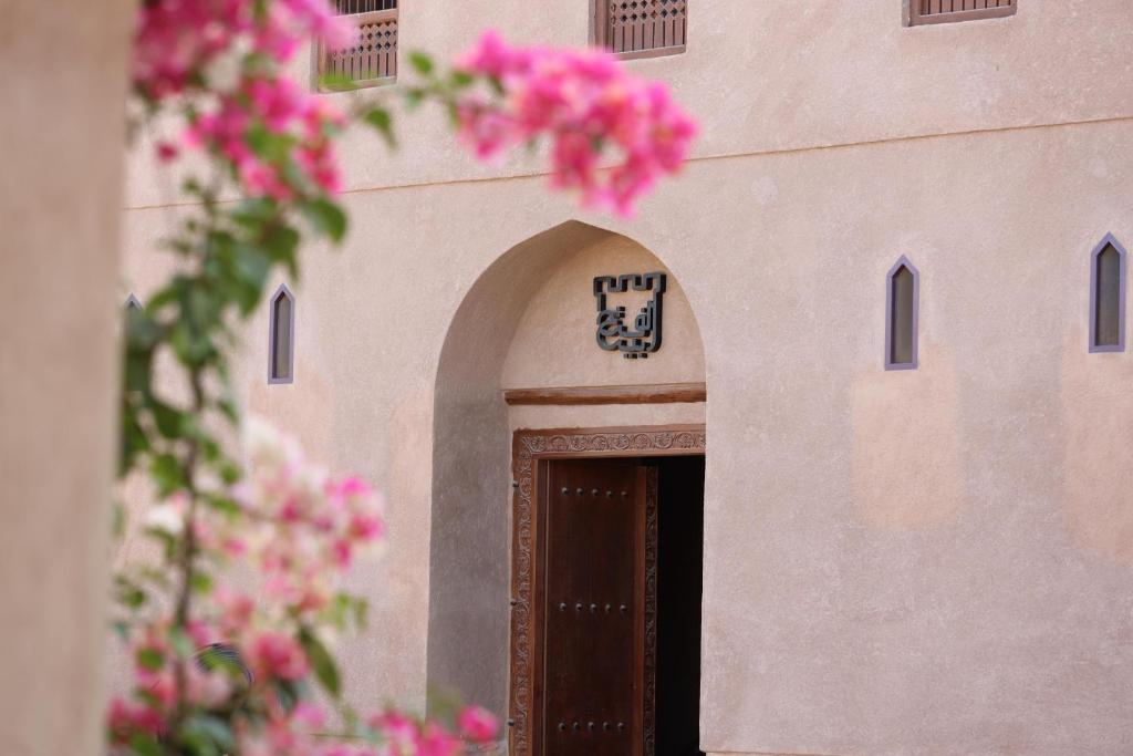 a building with a brown door with pink flowers at Beit Al Fateh بيت الفتح in Fatḩ Āl Bū Sa‘īd