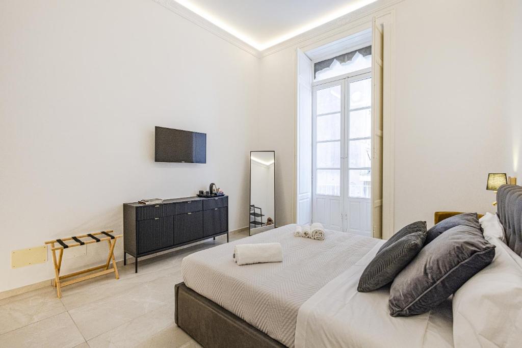 a white bedroom with a bed and a television at Dione Ortigia in Siracusa