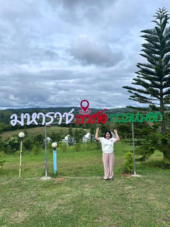a woman standing under a sign in a field at Sor Maharat Khaokho in Khao Kho
