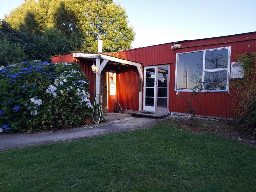 ein rotes Haus mit einer roten Tür und einem Hof in der Unterkunft Waitomo Farmstay - Morepork Cabin 7 in Waitomo Caves