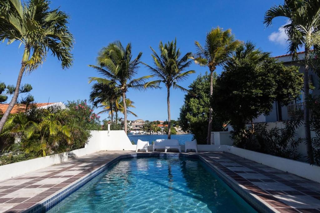 a swimming pool with chairs and palm trees at Aqualife Best view apartment in Willemstad