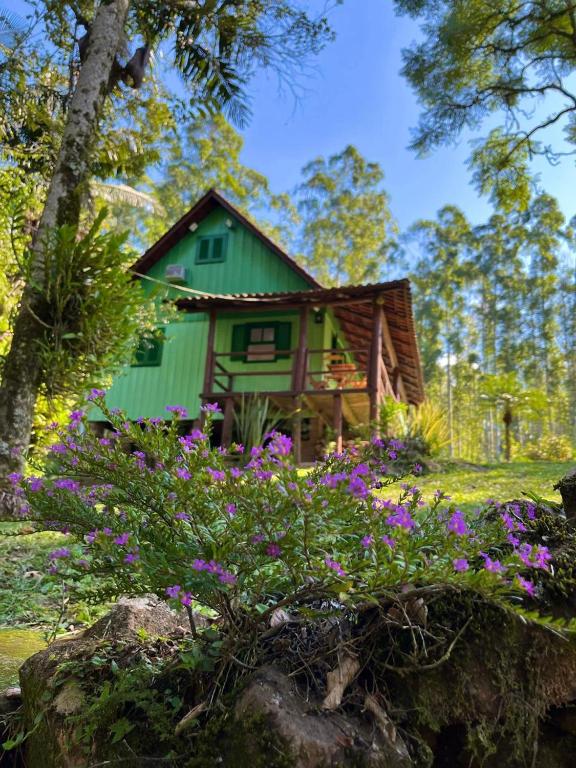 a green house with purple flowers in front of it at Canto da cascata in Gramado