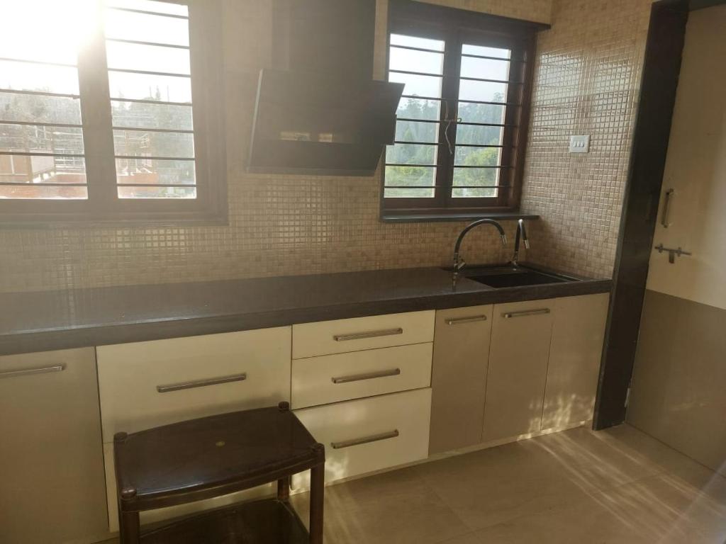 a kitchen with white cabinets and a sink and a stool at Nidha Home in Ooty