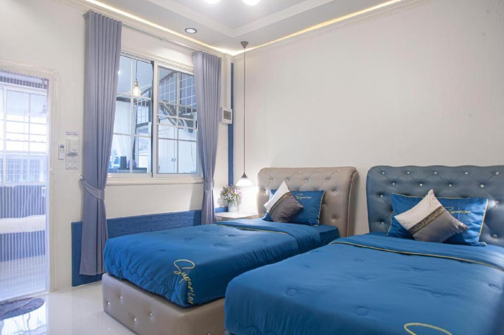 a bedroom with two beds with blue sheets and a window at Palm Sweet Hotel in Sathani Rot Fai