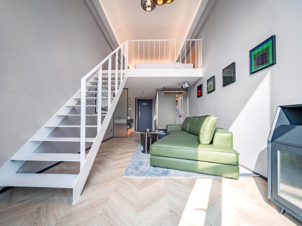 a living room with a staircase and a green chair at Chenfeng Hotel Wuhan Baishazhou Longhu Tianjie Branch in Wuhan