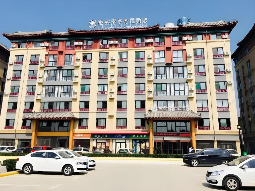 ein großes Gebäude mit auf einem Parkplatz abgestellten Autos in der Unterkunft GreenTree Inn Qufu High Speed Railway Station in Qufu