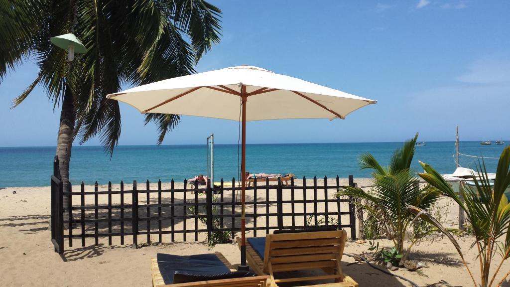 a beach with two chairs and an umbrella on the beach at Etnico Surf Resort in Arugam Bay