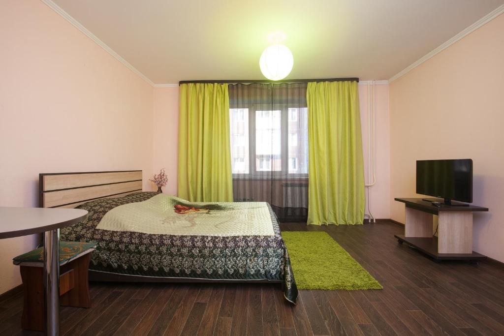 a bedroom with a bed with green curtains and a television at Adel Hotel in Krasnoyarsk