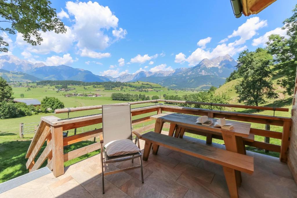 a wooden table and chair on a balcony with mountains at Chalet Die Mühle in Saalfelden am Steinernen Meer