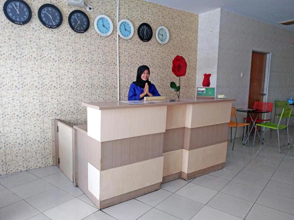 a woman sitting at a counter in a room with clocks on the wall at Wisma Jampea in Makassar
