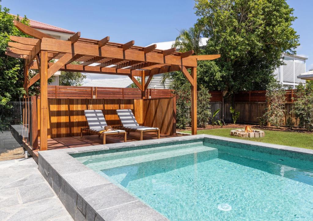 a swimming pool with a wooden pergola and two chairs next to a swimming at Mariners Rest in Yamba