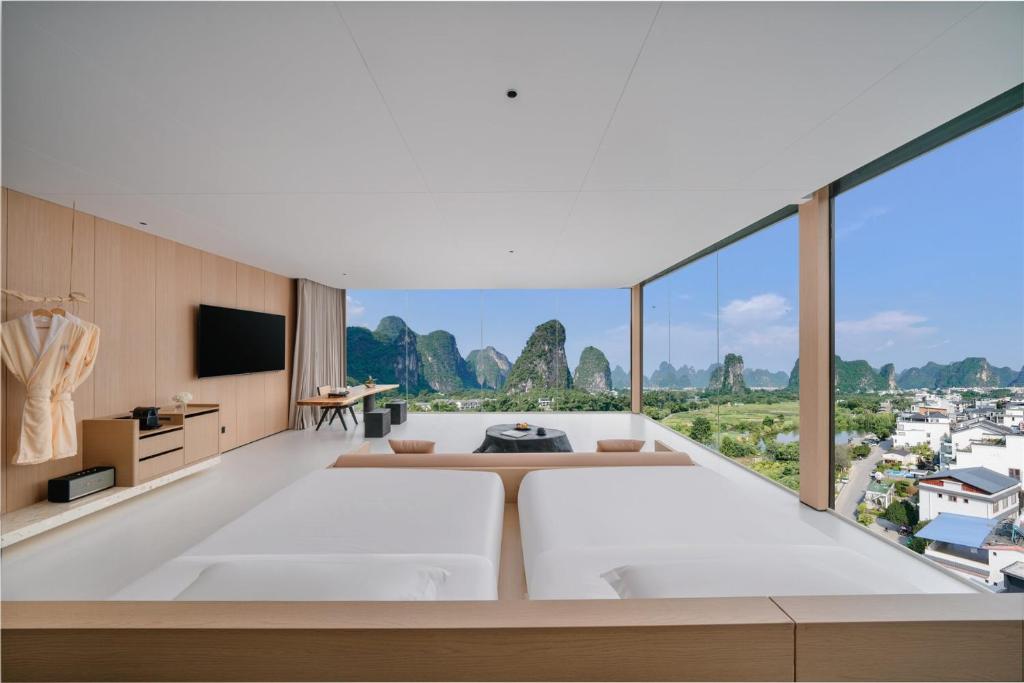 ein Schlafzimmer mit großem Bett und großen Fenstern in der Unterkunft Shuitiao Boli Hotel (Yangshuo Shili Gallery Yulonghe Branch) in Gaotian