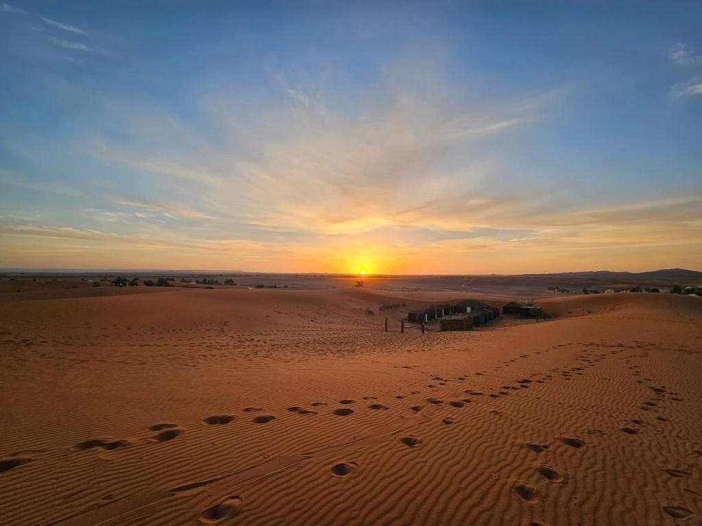 a sunset in the desert with footprints in the sand at Family Berber Camp in Merzouga