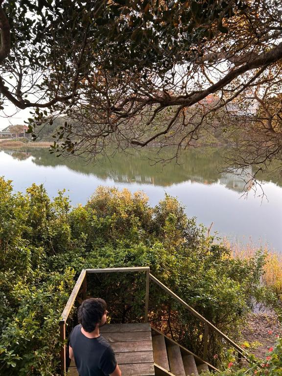 a man standing on a stairs near a lake at Explore River Cottage Ocean View in Seafield