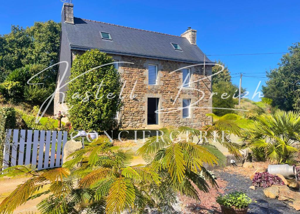 ein altes Steinhaus mit Zaun und Palmen in der Unterkunft Chez Jeanne, maison en pierre de pays avec jardin in Plougonver
