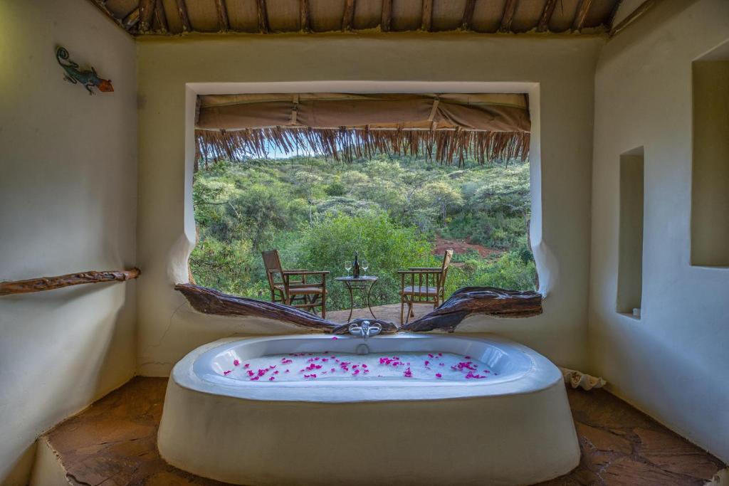 a bath tub in a room with a large window at Private bush camp with pool cottages tents - 2332 in Ilbisil