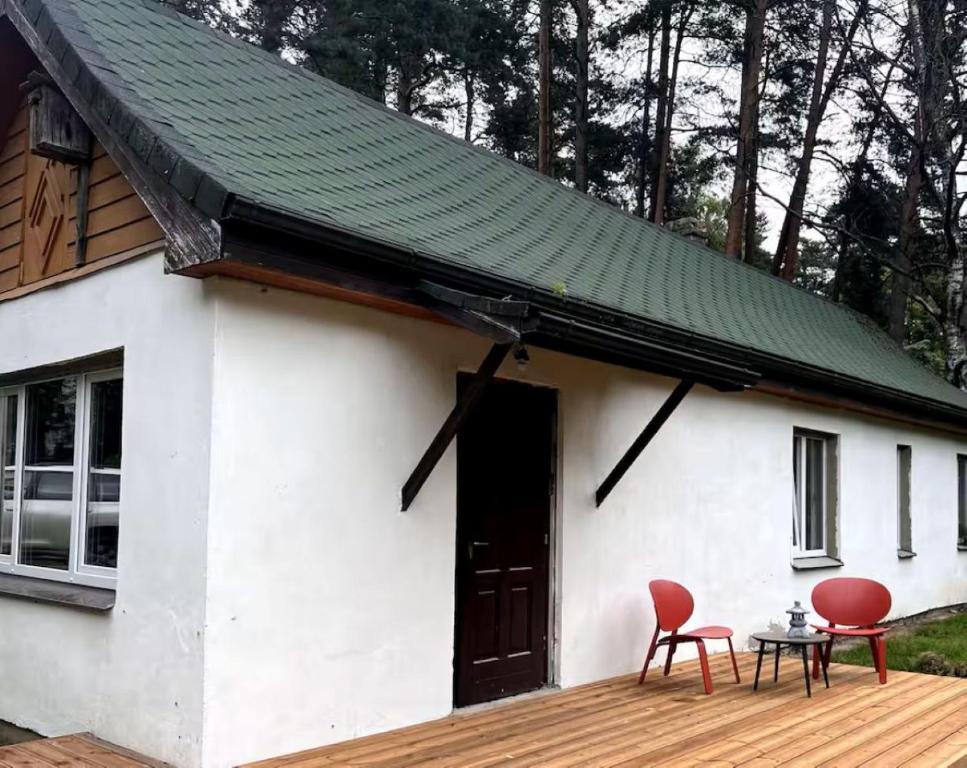 ein weißes Haus mit grünem Dach und zwei roten Stühlen in der Unterkunft Peace, Pines & Pure Air in Vangaži