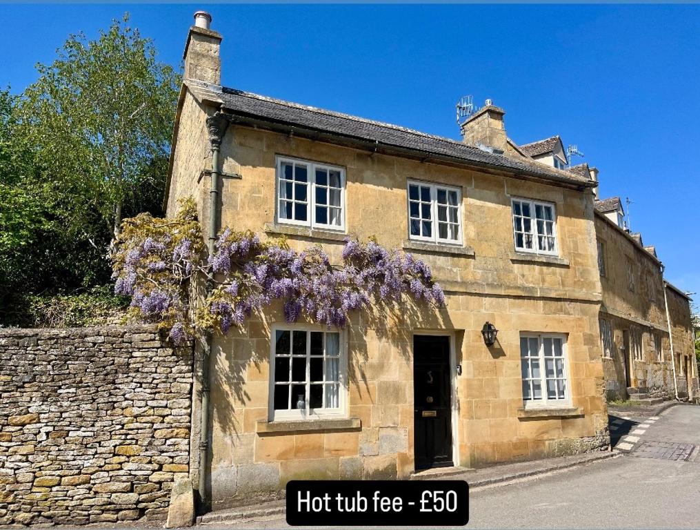 ein altes Steingebäude mit lila Blumen darauf in der Unterkunft The Carriage House in Blockley