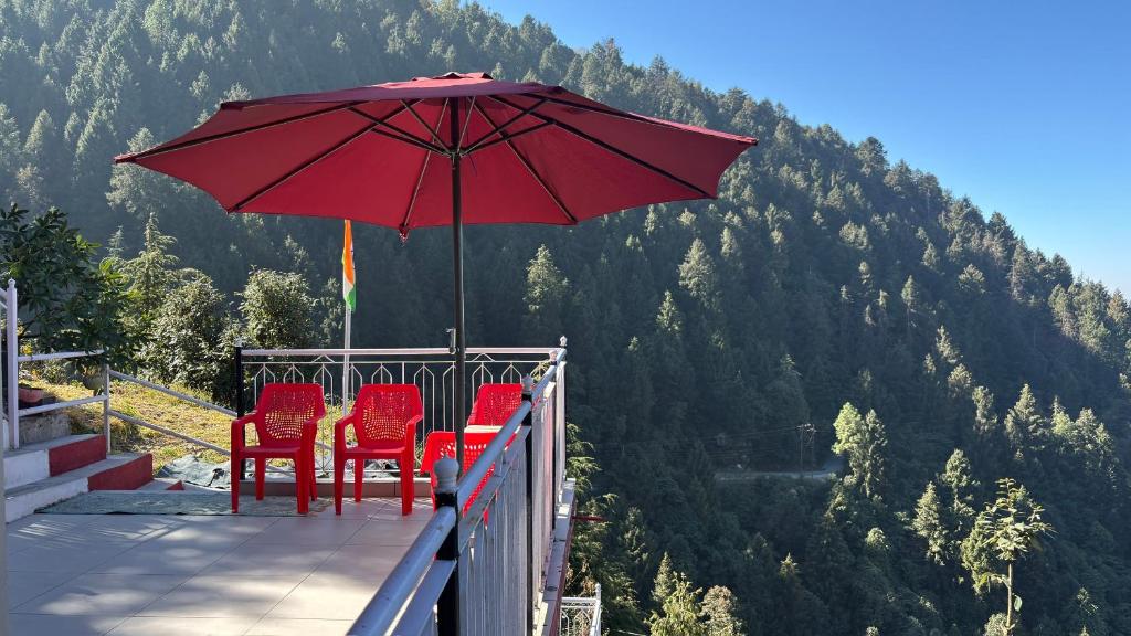 Eine Gruppe roter Stühle und ein Sonnenschirm auf einem Balkon in der Unterkunft FORTUNE HEIGHTS DALHOUSiE in Dalhousie