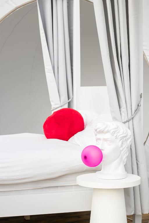 a white bed with a red pillow and a red ball at Barn bubble in Maidstone